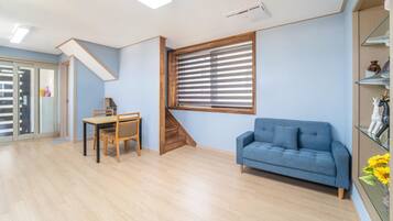 Una habitación con un sofá azul, una mesa de comedor de madera con sillas, una escalera y una ventana con persianas.