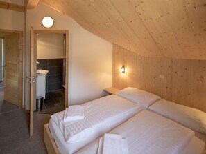 Une chambre avec deux lits, un plafond en bois, un luminaire rond et une salle de bain visible à travers une porte ouverte.