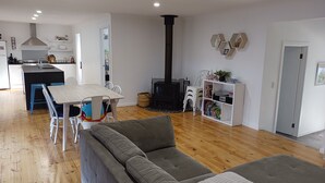 Un salon moderne avec un canapé gris, une table à manger avec des chaises, un coin cuisine avec des meubles blancs et une cheminée noire.