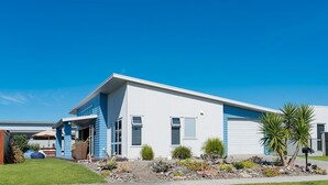 Une maison moderne à deux étages, dotée d’un garage, d’un jardin bien entretenu et surplombant un ciel d’un bleu éclatant.