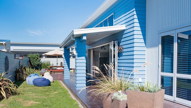 Une maison moderne à l’extérieur bleu, dotée d’un patio couvert avec des meubles d’extérieur et d’un jardin bien entretenu.