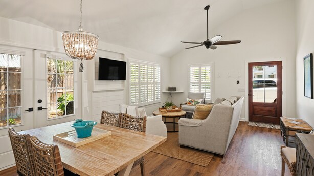 A spacious living area with a dining table, wicker chairs, a sofa, and a ceiling fan. - Stunning backyard oasis nestled between pier/village and beach - SSI Sunshine (St Simons Island)