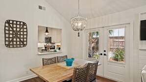 A dining area with a wooden table, wicker chairs, a chandelier, and a view of a backyard through a sliding door. - Stunning backyard oasis nestled between pier/village and beach - SSI Sunshine (St Simons Island)