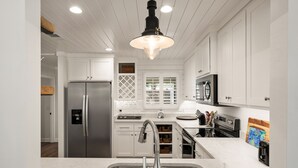 A modern kitchen with white cabinetry, stainless steel appliances, and a marble countertop. - Stunning backyard oasis nestled between pier/village and beach - SSI Sunshine (St Simons Island)