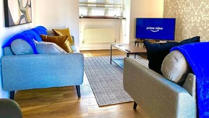 Un soggiorno moderno con un divano grigio, una poltrona blu e una televisione che mostra 'prime video'.