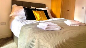 Un letto rifatto con cura, una coperta a motivi e vari cuscini, con asciugamani piegati sul letto.