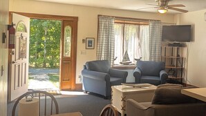 Una sala de estar acogedora con una mesa de comedor de madera, dos sofás, un televisor y un ventilador de techo.