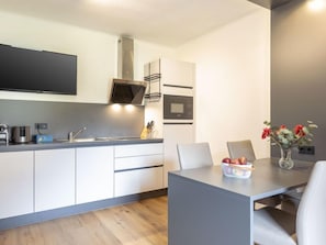 A modern kitchen with white cabinets, a flat-screen TV, a microwave, and a dining area with a table and chairs.