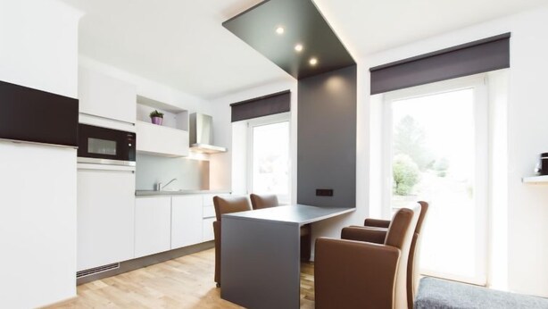 A modern kitchen with white cabinets, a central island, and a dining area with brown chairs.