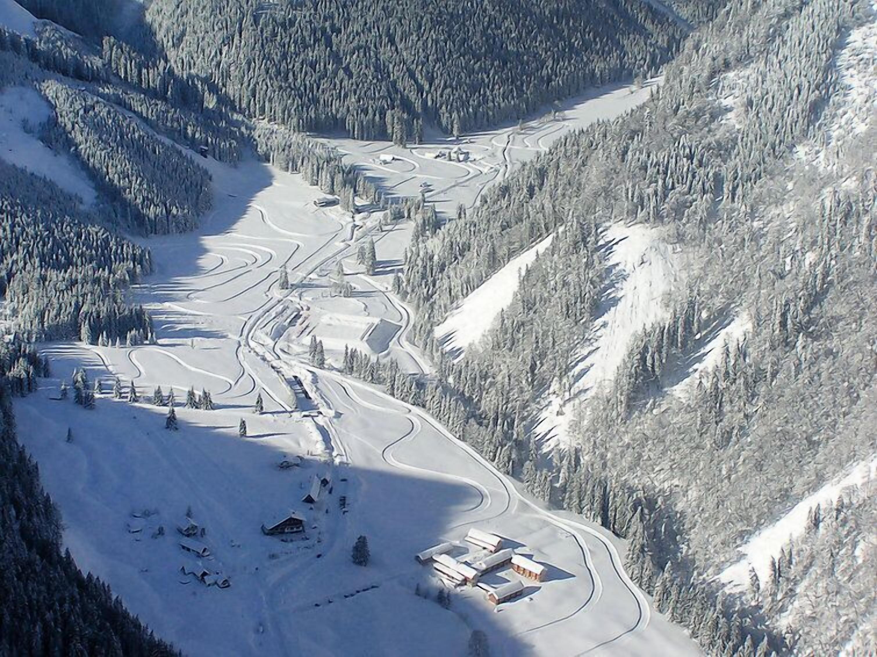 A snow-covered ski resort with winding roads, a lodge, and forested mountains.