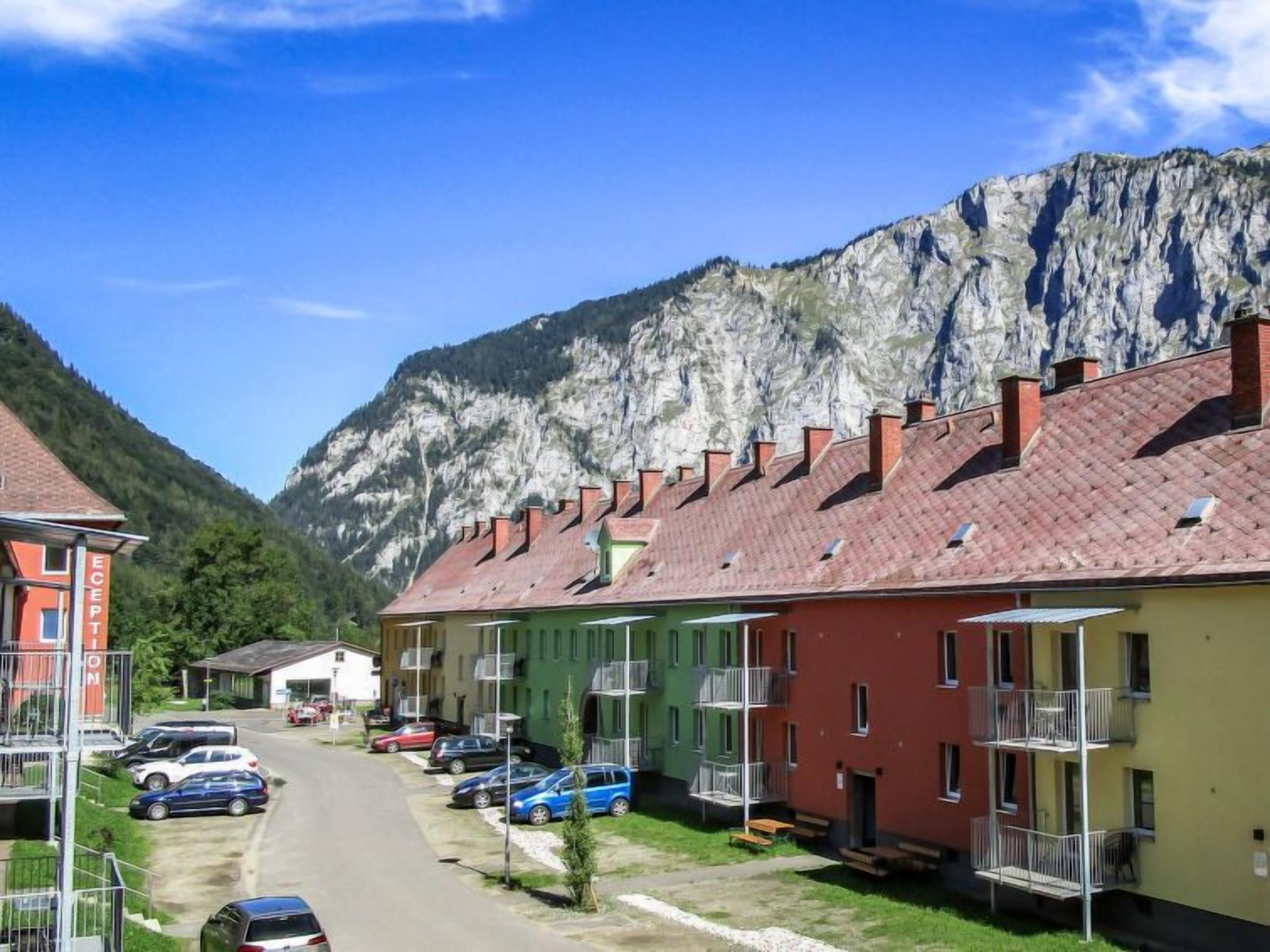 Une rangée de bâtiments colorés dotés de balcons, un espace de stationnement et un paysage montagneux en arrière-plan.