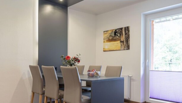 A dining area with a table and chairs, a vase with flowers, and a painting on the wall.