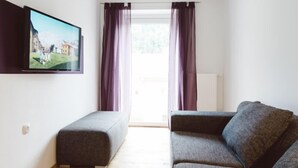 A modern living room with a grey sofa, a bench, and a flat-screen TV mounted on the wall.