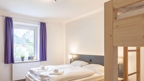A bedroom with a wooden bed, a window with purple curtains, a radiator, and a view of mountains.