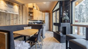 Un interno moderno con zona pranzo in legno, sedute rivestite in tessuto nero e un camino.