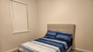 Une chambre à coucher avec un lit, une fenêtre avec des stores et un sol recouvert de moquette.