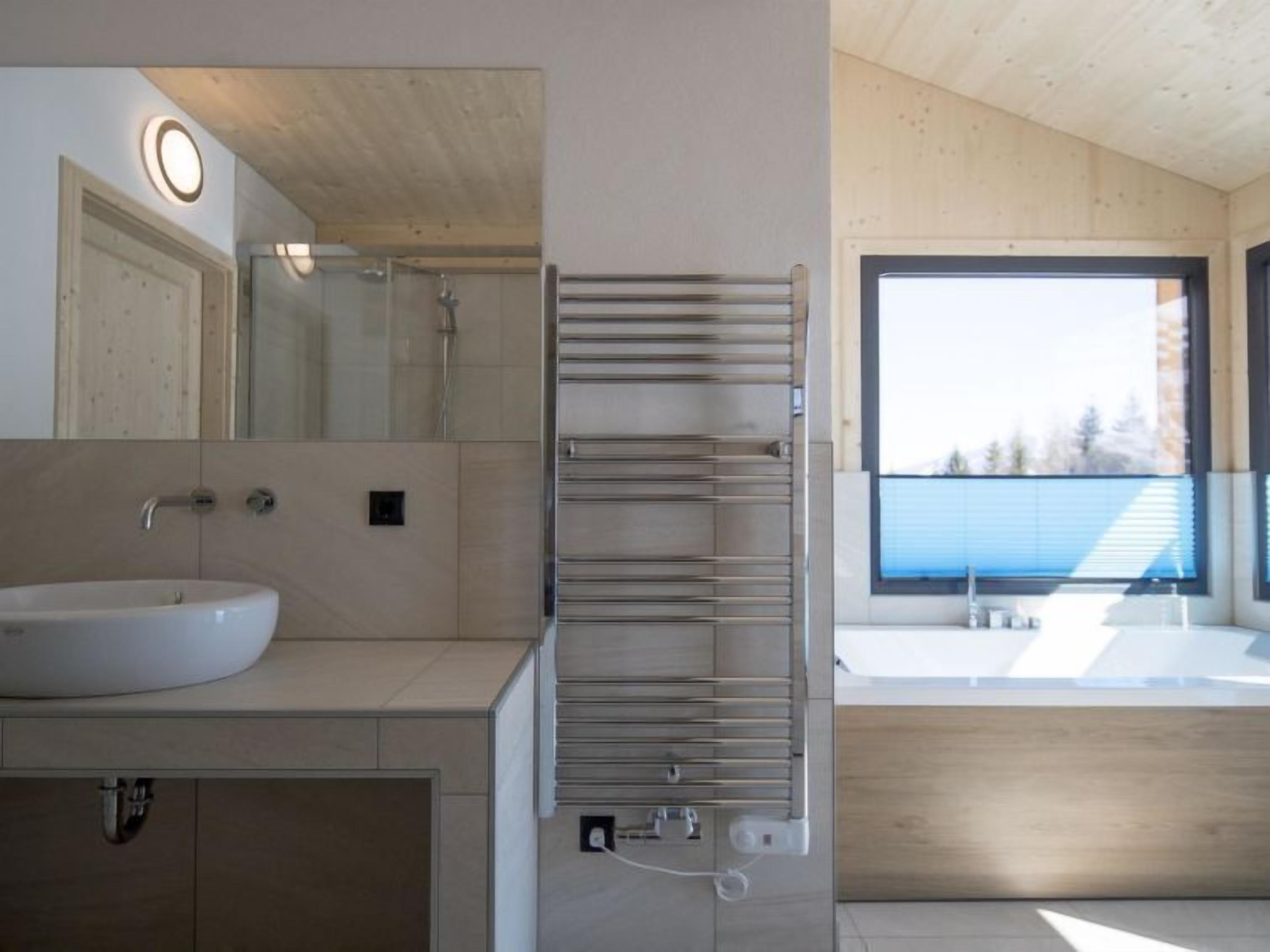A modern bathroom with a large mirror, a sink, a towel rack, and a window providing a view of the outdoors.