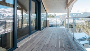 Um deck de madeira com guarda-corpos de vidro com vista para uma paisagem montanhosa.