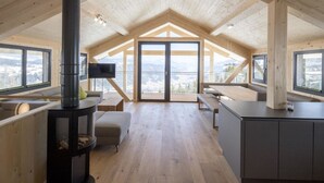 Um quarto amplo no sótão, com teto alto, vigas de madeira, lareira, uma janela grande e vista para as montanhas.