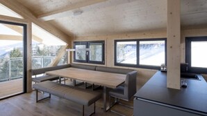 Uma cabana moderna de madeira com área de refeições, assentos em banco e grandes janelas com vista para as montanhas.