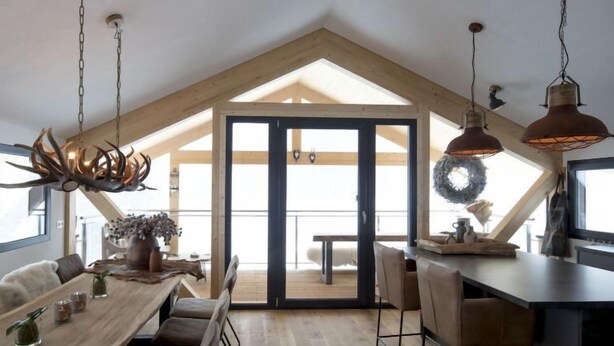 A modern loft with a high ceiling, a wooden dining table, and a kitchen area with bar stools. - Premium # 01 IR-Sauna&Sprudelpool aussen by Interhome (Pichl)