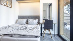 A bedroom with a bed, a desk, and a chair. There is a window with a view of a building outside. - Superior # 03 Sauna&Sprudelwanne innen by Interhome (Pichl)