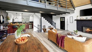 A spacious living area with a high ceiling, a staircase, a fireplace, and a kitchen in the background.