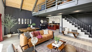 A spacious living area with a high ceiling, a wooden staircase, a dining area, and a kitchen.