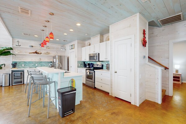 Kitchen with central island, sink, and stools, featuring white cabinetry and stainless steel appliances.