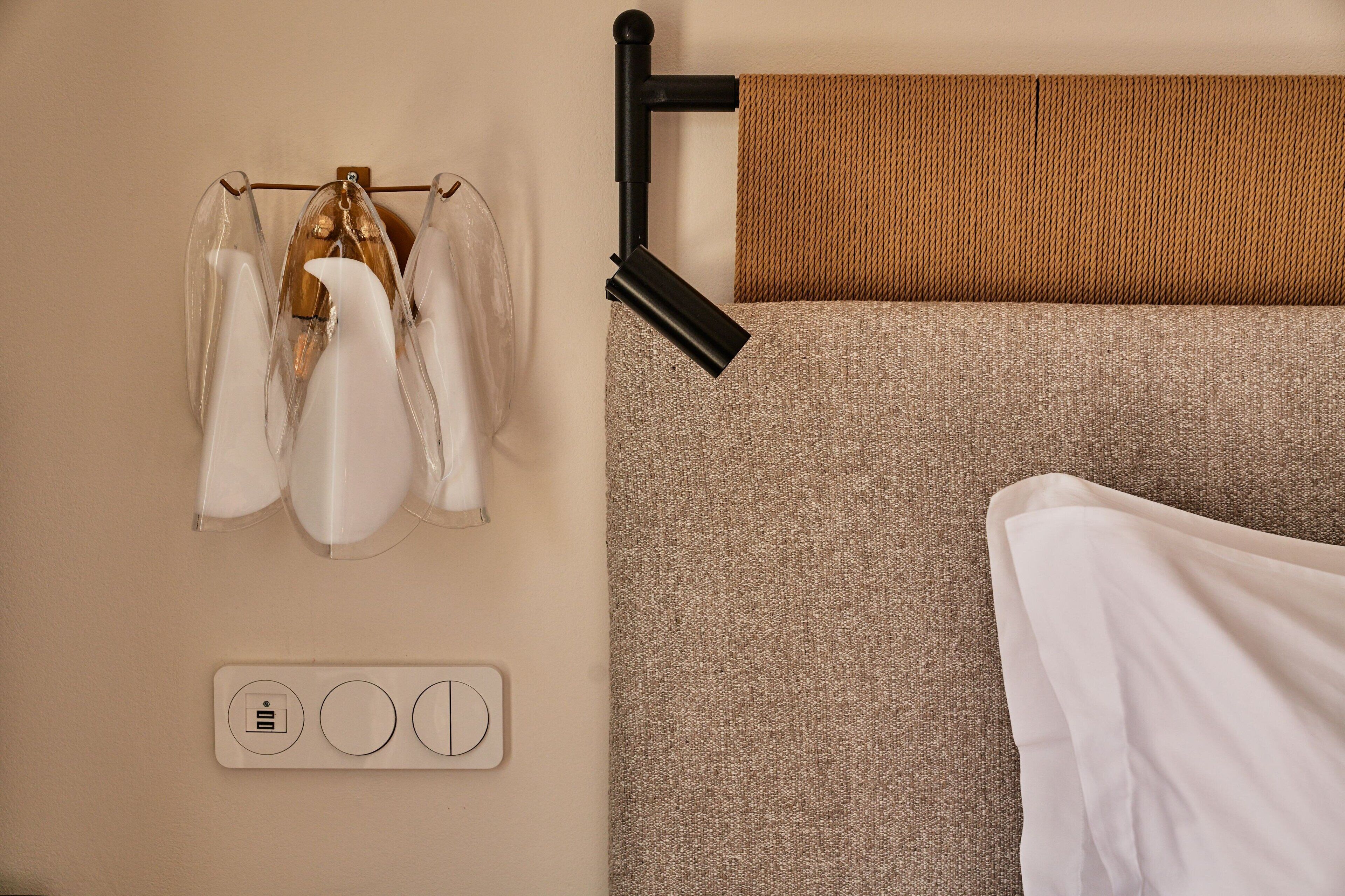 A neatly arranged hotel room with a bed, a towel rack with towels, and a wall-mounted control panel.