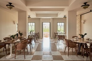 A spacious dining area with checkered flooring, multiple tables set for dining, and natural light from large windows.