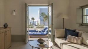 A modern living room with a sofa, a small table with a decorative bowl, and a view of a balcony with a blue sofa and palm trees. - Cosme, A Luxury Collection Resort, Paros (Paros)