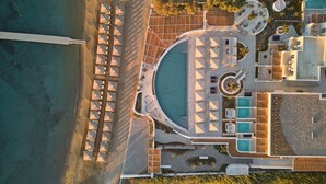 An aerial view of a resort with a large pool, multiple sun loungers, and a beach area. - Cosme, A Luxury Collection Resort, Paros (Paros)