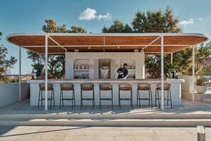 A modern outdoor bar area with a wooden canopy, white bar counter, and wicker chairs.