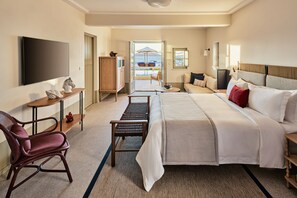 A hotel room with a large bed, a desk, a chair, a TV, and a view of the sea.