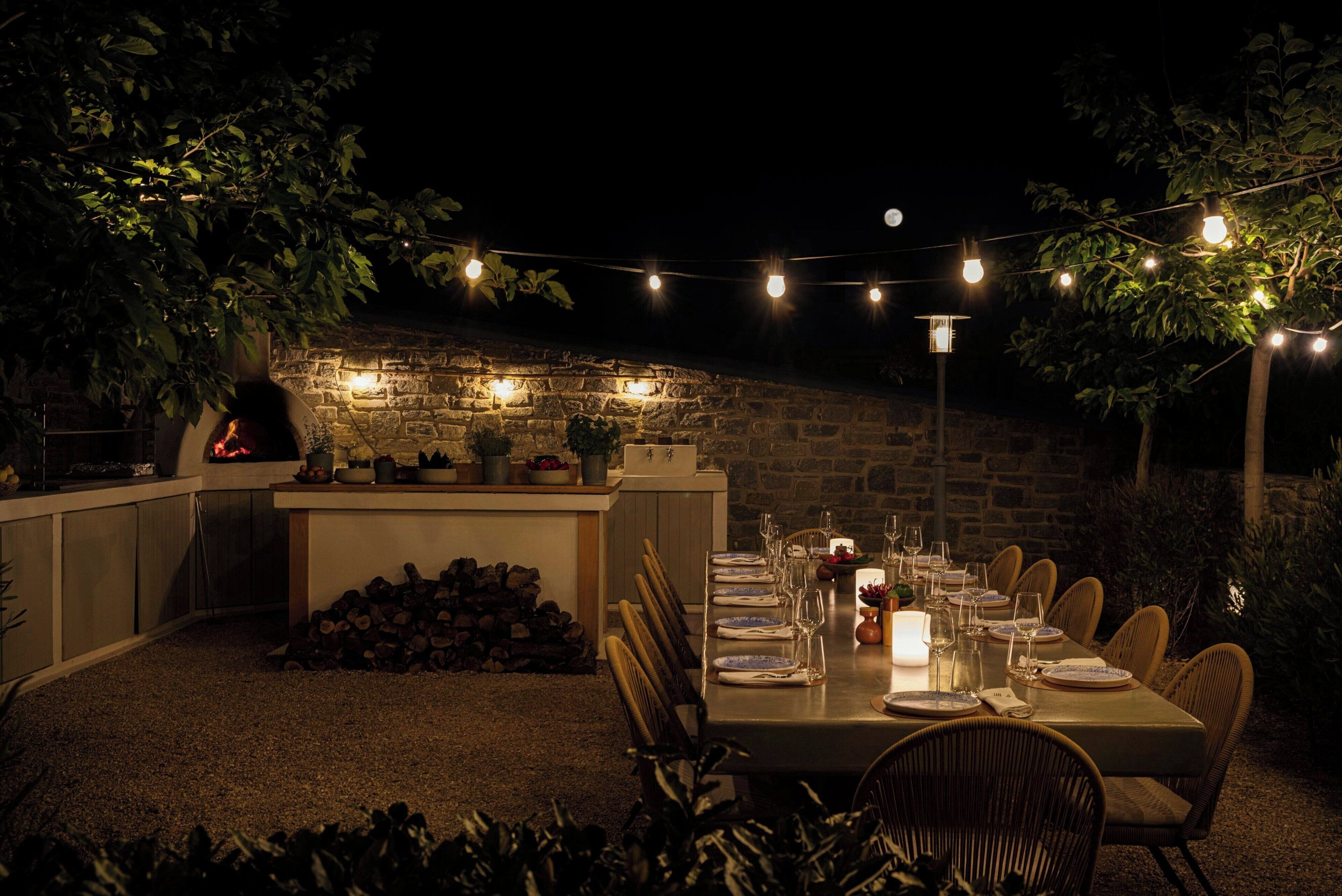 Un área de comedor al aire libre con una pared de piedra, luces colgantes y una chimenea.