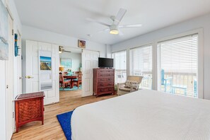A bedroom with a bed, a television, a dresser, a chair, and a balcony with a view.