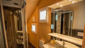Kylpyhuoneessa on lasiseinällä varustettu suihku, peilillä varustettu pesuallas ja peilin yläpuolella oleva ikkuna.