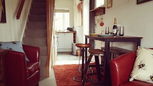 A cozy living room with a staircase, a dining area with a table set for two, and a kitchen in the background. - Charming 1-bed Maisonette With Mountain View (Pontypool)
