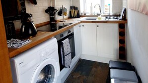 A compact kitchen with a washing machine, a stove, and a sink. - Charming 1-bed Maisonette With Mountain View (Pontypool)
