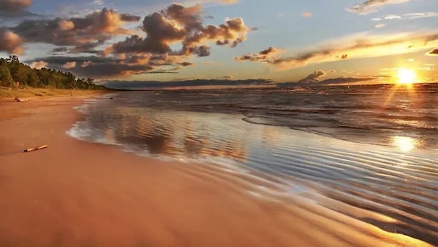 A beach with a sunset, calm water, and a distant shoreline.
