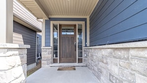 A house entrance with a dark wooden door, stone steps, and a concrete porch.