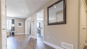 A hallway with wooden flooring, a large mirror, and a vent on the wall.