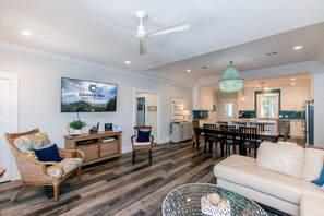 Un salon spacieux avec un canapé blanc, des fauteuils en osier, une table basse en verre et un coin repas comprenant une table et des chaises blanches.