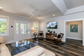 A spacious living room with a ceiling fan, a television mounted on the wall, and a large window.