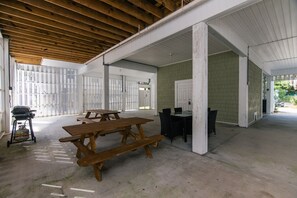Un espace patio intérieur couvert, équipé de tables et de chaises pour pique-nique, d’un barbecue et d’une bouteille de gaz.