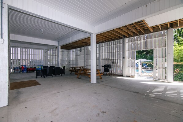 An indoor space with a high ceiling, open areas, and a view of a pool outside.