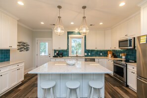 A kitchen with white cabinets, a central island with stools, stainless steel appliances, and a green-tiled backsplash.