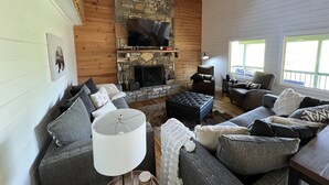 Ein gemütliches Wohnzimmer mit Kamin aus Stein, einem großen Flachbildfernseher und einer komfortablen Sitzecke mit Sofas und Couchtisch.