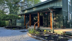 Ein modernes Haus mit einer überdachten Veranda, Holzstufen und einer Schotterzufahrt.